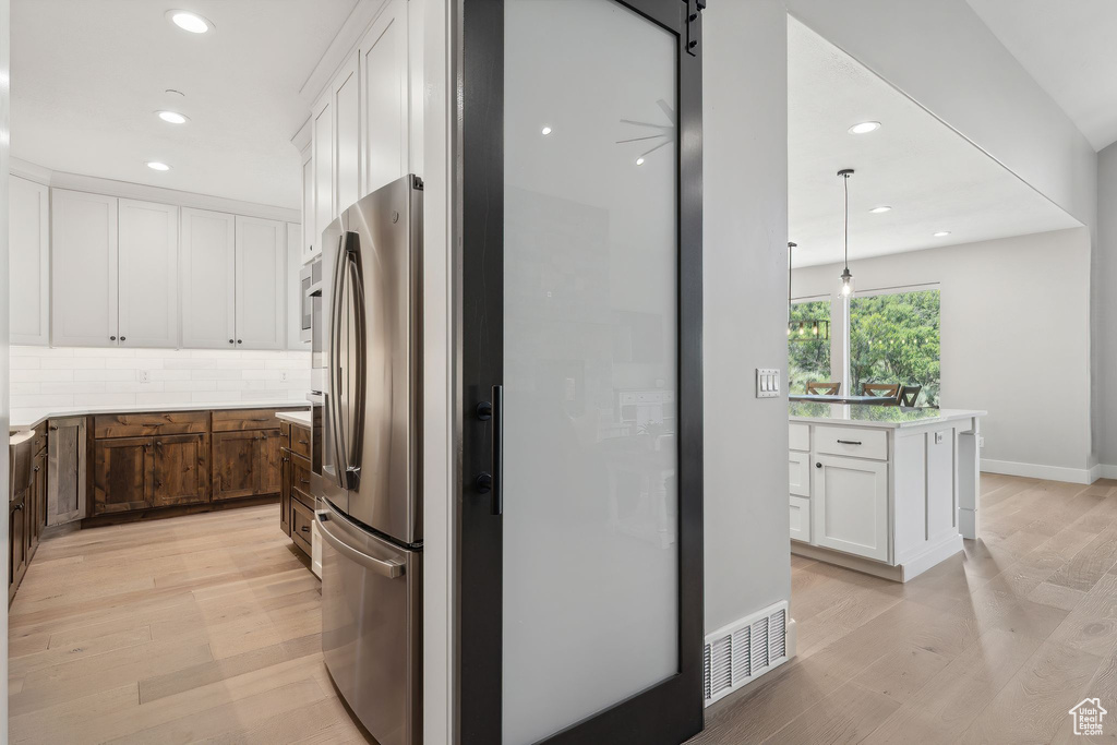 Kitchen featuring stainless steel refrigerator, light hardwood / wood-style floors, decorative backsplash, an island with sink, and white cabinetry