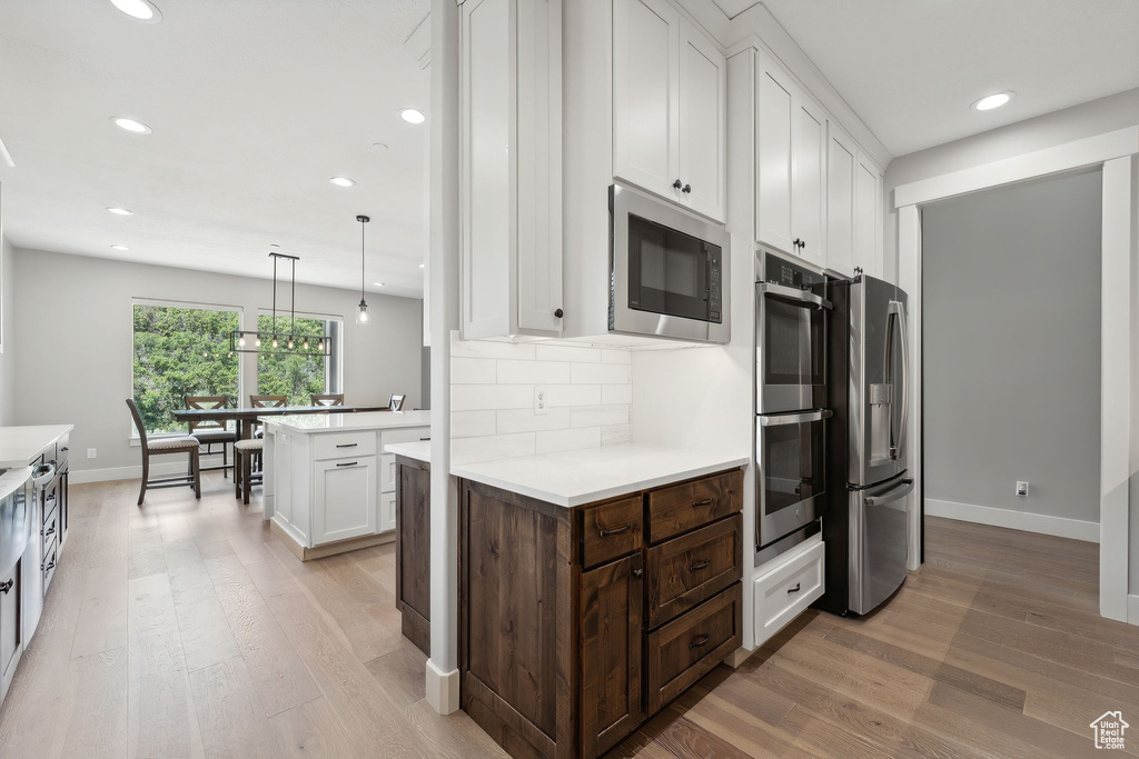 Kitchen with decorative light fixtures, tasteful backsplash, stainless steel appliances, a center island, and light hardwood / wood-style flooring