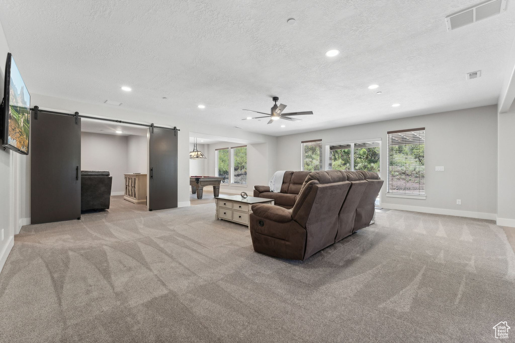 Carpeted living room with a textured ceiling, ceiling fan, a barn door, and billiards