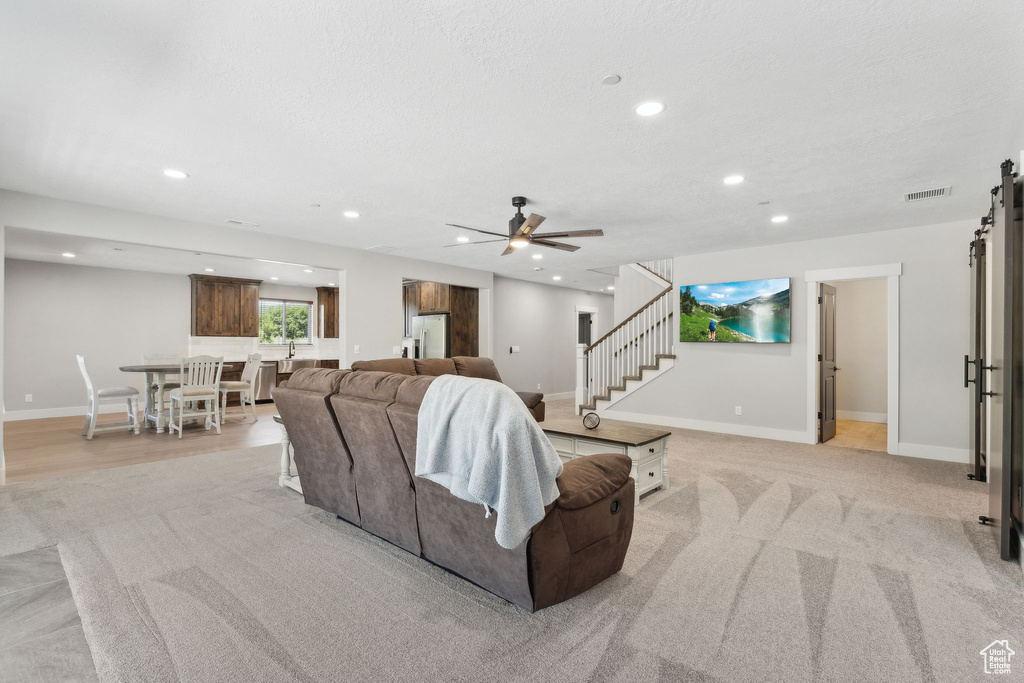 Living room with light carpet, a barn door, and ceiling fan