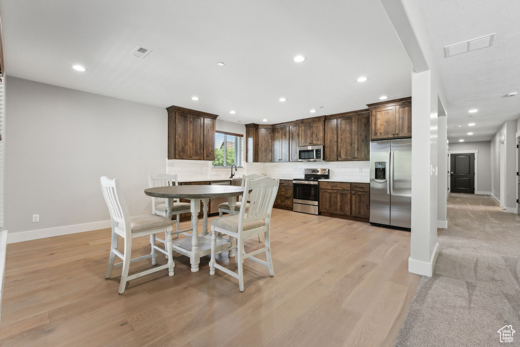 Kitchen featuring stainless steel appliances, backsplash, dark brown cabinets, and light wood-type flooring