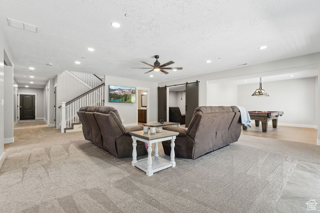 Carpeted living room featuring a textured ceiling, ceiling fan, a barn door, and billiards