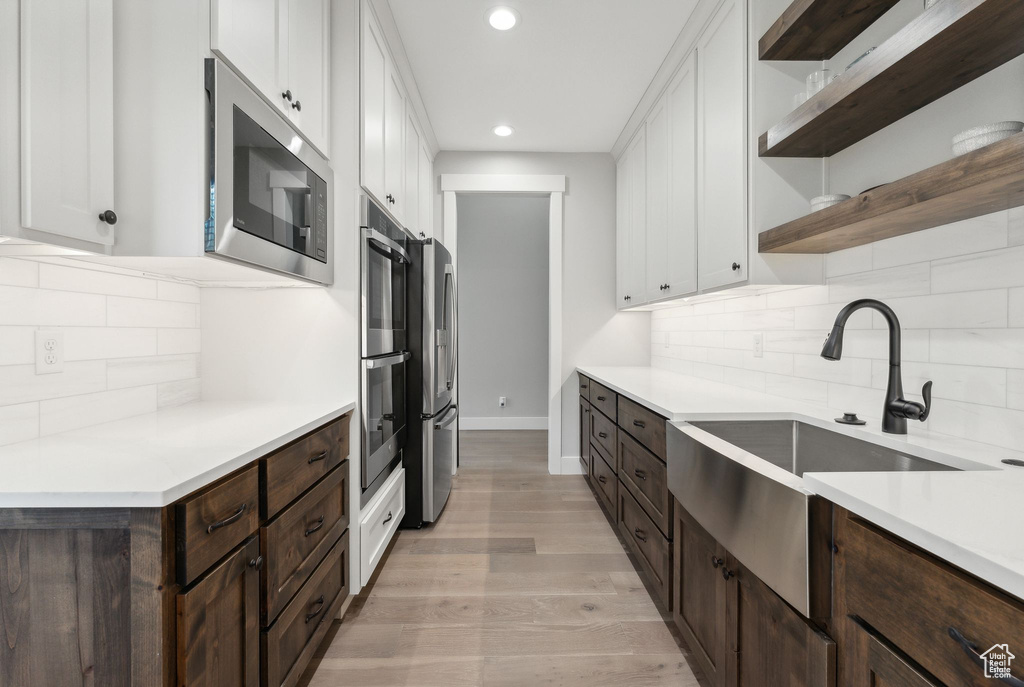 Kitchen featuring stainless steel appliances, white cabinets, dark brown cabinets, decorative backsplash, and light wood-type flooring