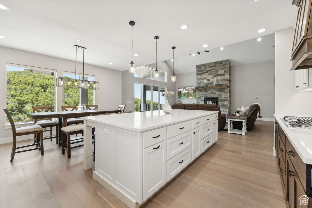 Kitchen with white cabinetry, decorative light fixtures, a fireplace, a kitchen island, and light hardwood / wood-style floors