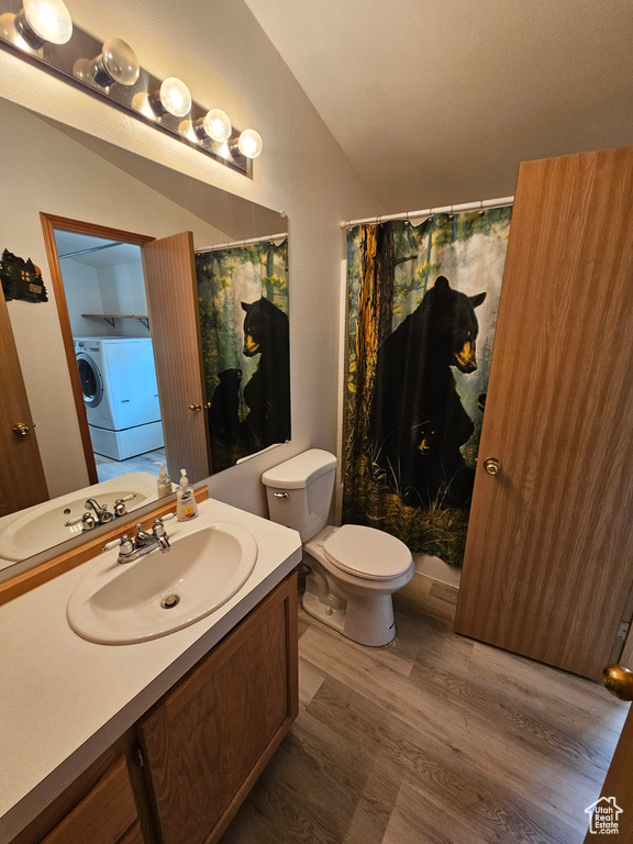 Bathroom featuring lofted ceiling, toilet, vanity, washer / dryer, and wood-type flooring