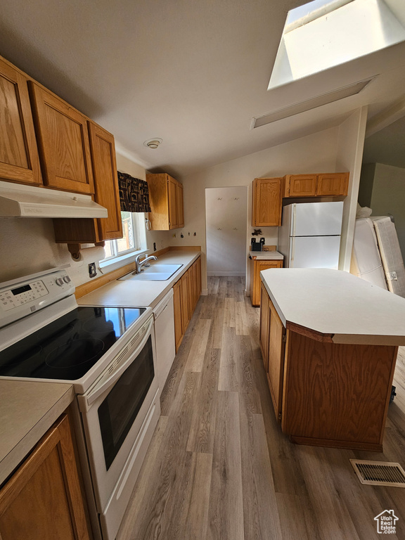 Kitchen featuring lofted ceiling with skylight, hardwood / wood-style floors, white appliances, sink, and a center island