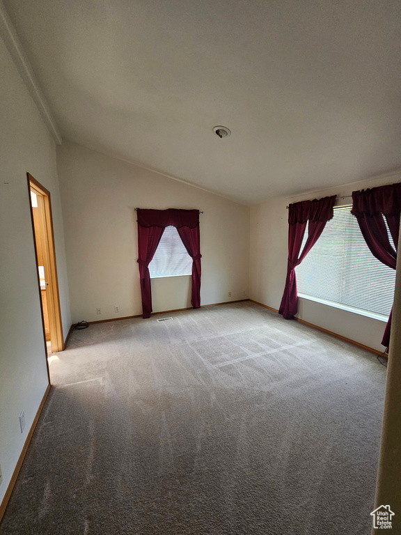 Carpeted spare room featuring ornamental molding and vaulted ceiling