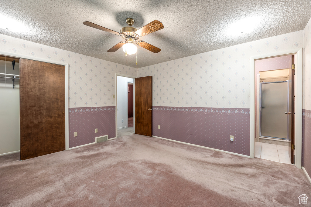 Unfurnished bedroom featuring a closet, a textured ceiling, light colored carpet, and ceiling fan