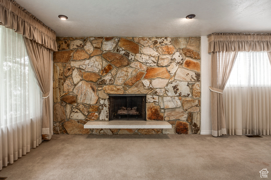 Unfurnished living room featuring carpet flooring, a textured ceiling, and a stone fireplace