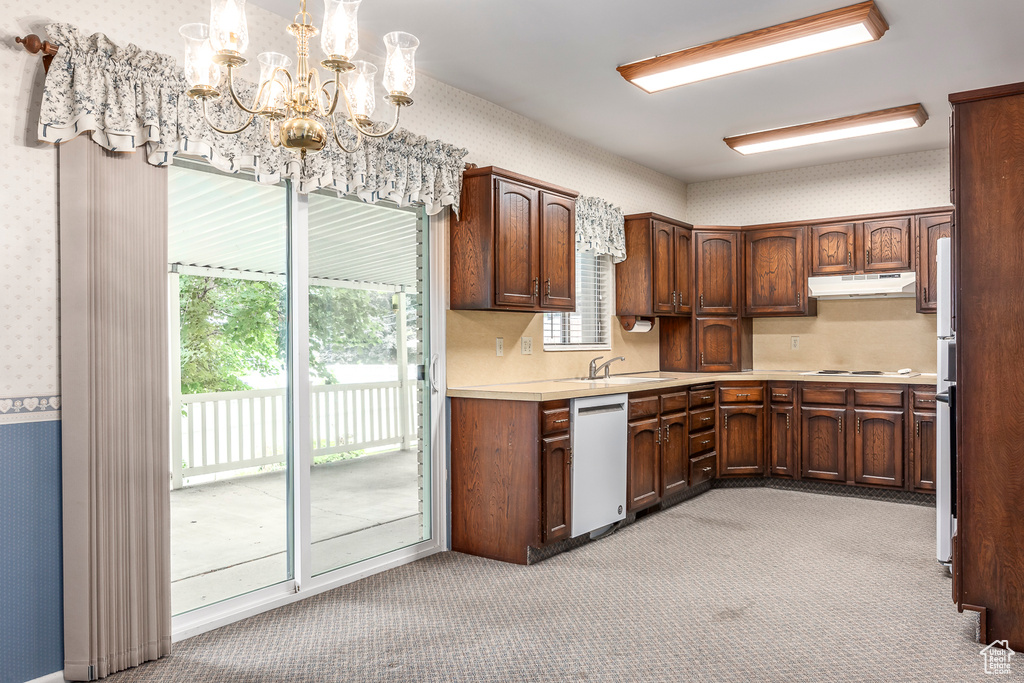 Kitchen with white appliances, an inviting chandelier, sink, hanging light fixtures, and light carpet