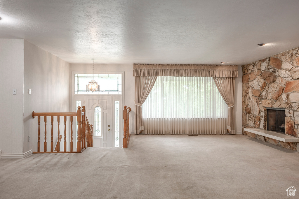 Unfurnished living room with a stone fireplace, a notable chandelier, carpet floors, and a textured ceiling