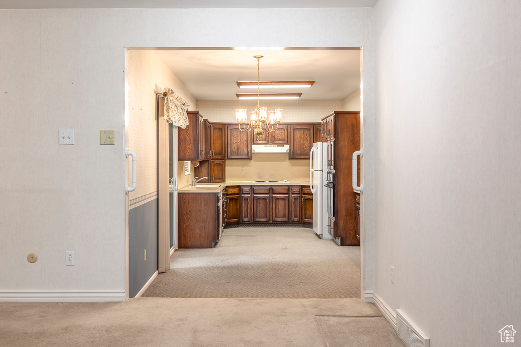 Kitchen with cooktop, decorative light fixtures, white fridge, an inviting chandelier, and light colored carpet