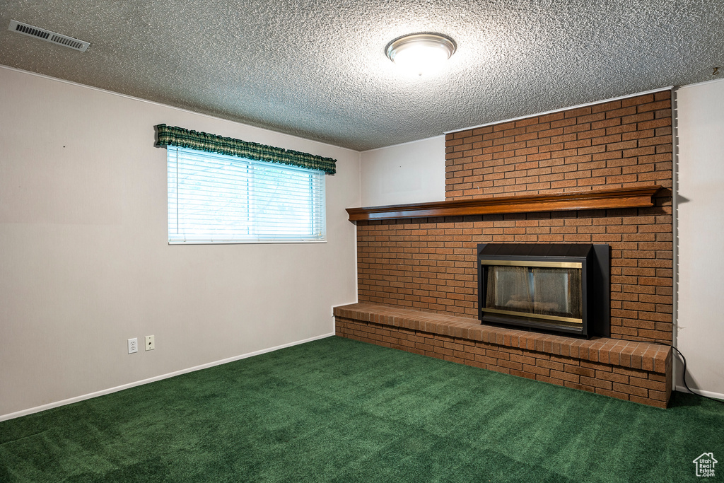 Unfurnished living room featuring brick wall, a fireplace, dark colored carpet, and a textured ceiling