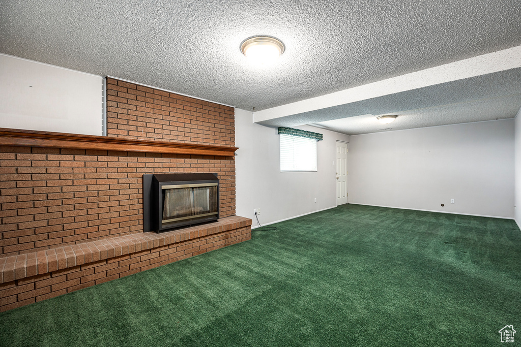 Unfurnished living room with a fireplace, dark carpet, brick wall, and a textured ceiling