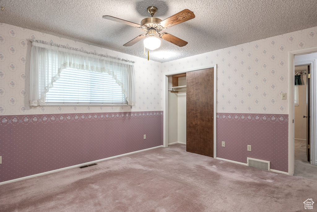 Empty room with carpet flooring, a textured ceiling, and ceiling fan