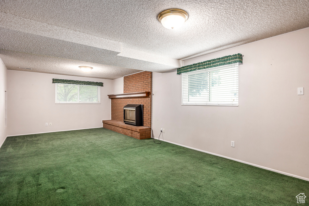 Unfurnished living room featuring brick wall, carpet flooring, a brick fireplace, and a textured ceiling