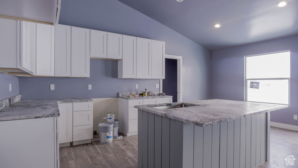 Kitchen featuring white cabinets, a center island, vaulted ceiling, and hardwood / wood-style floors