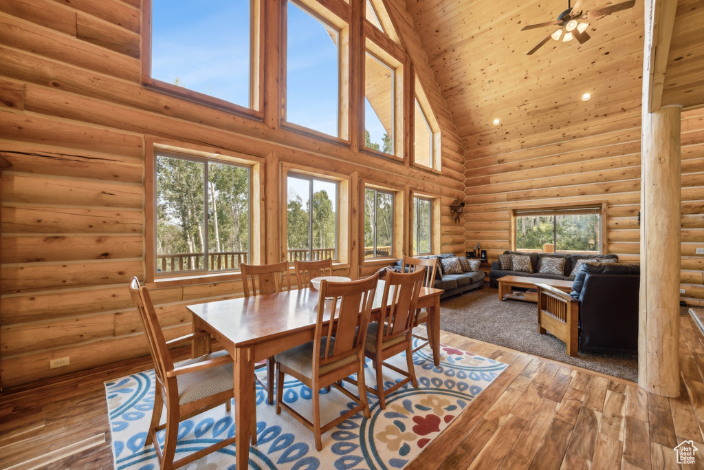 Dining area featuring high vaulted ceiling, ceiling fan, hardwood / wood-style flooring, and rustic walls