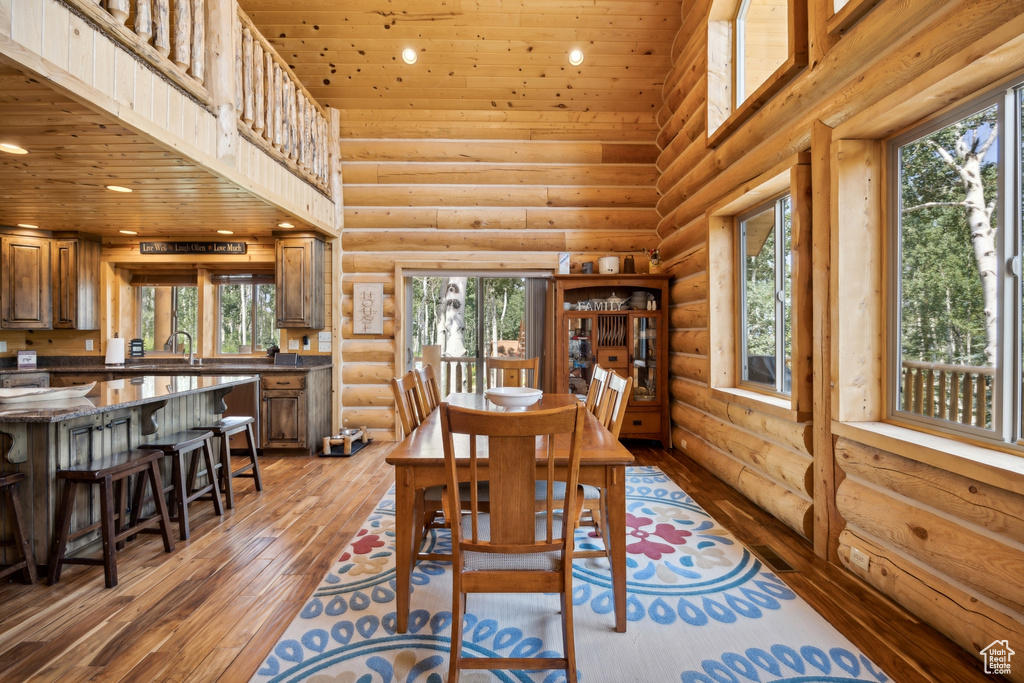 Dining area with hardwood / wood-style floors, plenty of natural light, rustic walls, and a towering ceiling