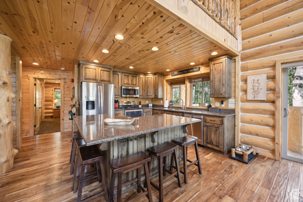 Kitchen featuring appliances with stainless steel finishes, wooden ceiling, light hardwood / wood-style flooring, and rustic walls