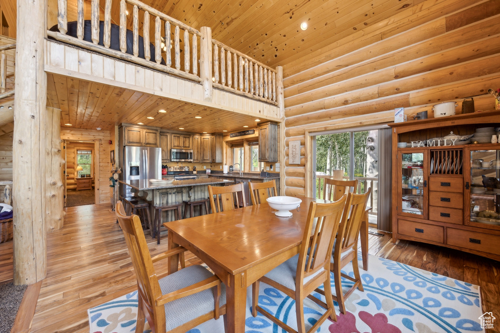 Dining space featuring light hardwood / wood-style flooring, a high ceiling, log walls, and wood ceiling