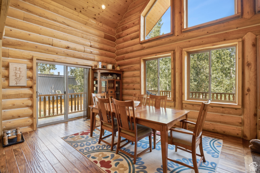 Dining room with light hardwood / wood-style flooring, log walls, and high vaulted ceiling