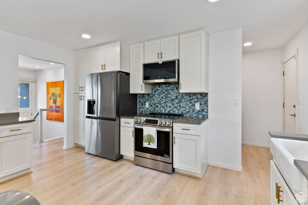 Kitchen with decorative backsplash, appliances with stainless steel finishes, light hardwood / wood-style flooring, and white cabinetry