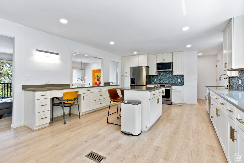 Kitchen with a breakfast bar area, stainless steel appliances, backsplash, light hardwood / wood-style floors, and white cabinetry