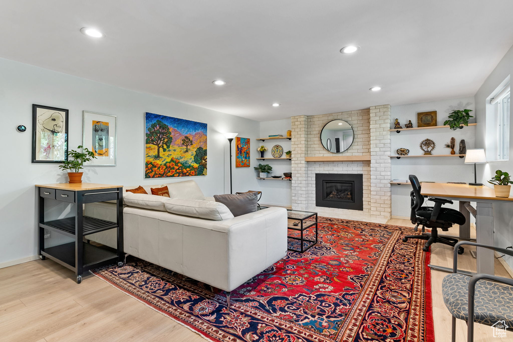 Living room featuring a fireplace, brick wall, and light wood-type flooring