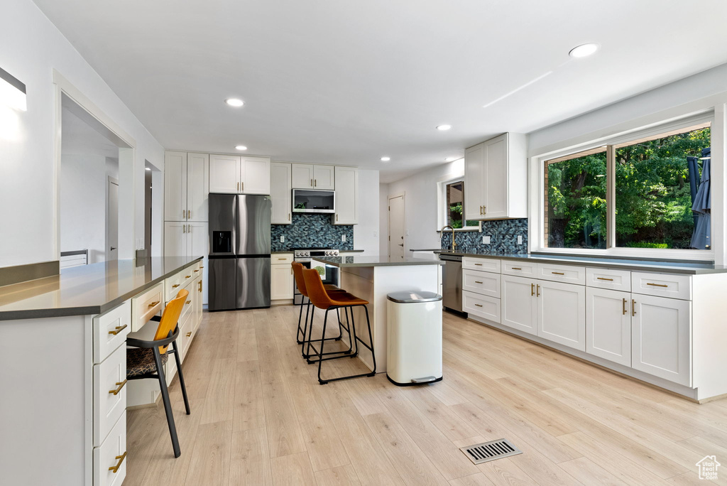 Kitchen featuring a kitchen bar, white cabinetry, light wood-type flooring, and stainless steel appliances