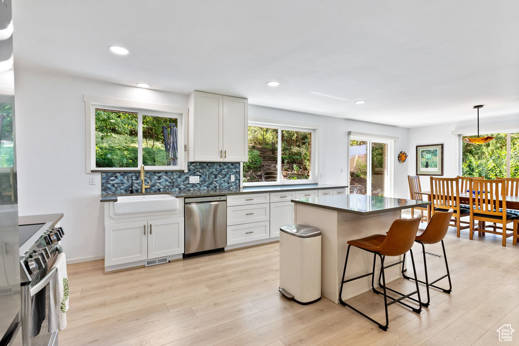 Kitchen featuring stainless steel appliances, decorative backsplash, white cabinets, sink, and light hardwood / wood-style floors