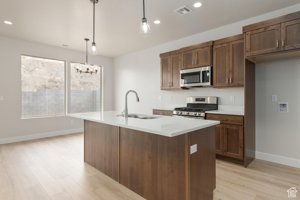 Kitchen featuring appliances with stainless steel finishes, sink, pendant lighting, light hardwood / wood-style floors, and a kitchen island with sink