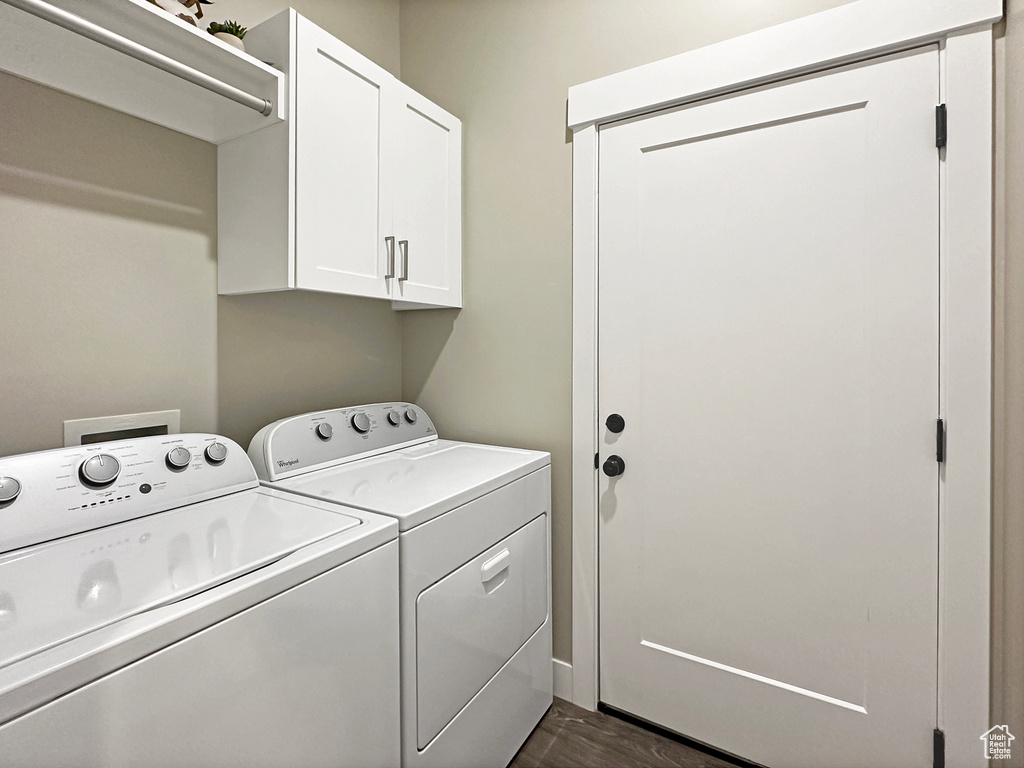 Clothes washing area featuring dark wood-type flooring, washer and clothes dryer, and cabinets