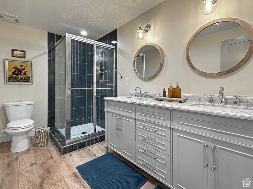 Bathroom with walk in shower, a textured ceiling, dual bowl vanity, toilet, and hardwood / wood-style flooring