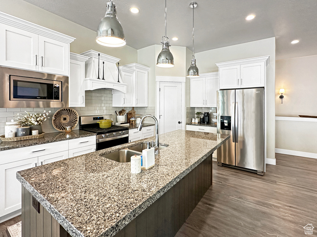 Kitchen with a kitchen island with sink, dark hardwood / wood-style flooring, stainless steel appliances, and backsplash