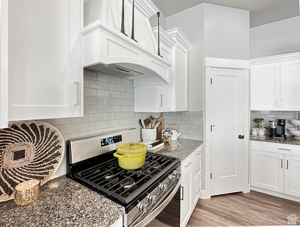 Kitchen featuring white cabinets, light hardwood / wood-style floors, backsplash, stainless steel gas range, and custom exhaust hood