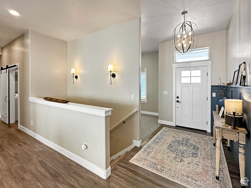 Foyer with an inviting chandelier, dark wood-type flooring, and a barn door