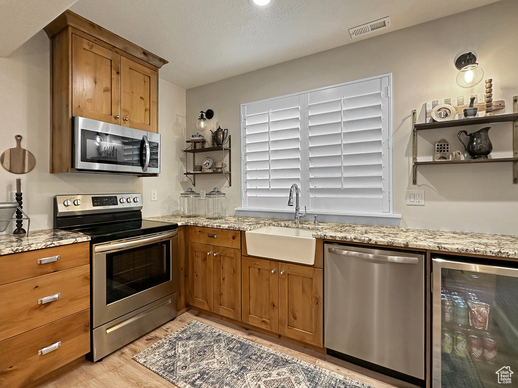 Kitchen featuring stainless steel appliances, sink, light hardwood / wood-style floors, light stone countertops, and beverage cooler