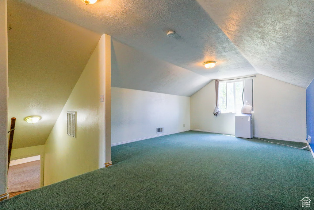 Bonus room featuring carpet flooring, lofted ceiling, and a textured ceiling