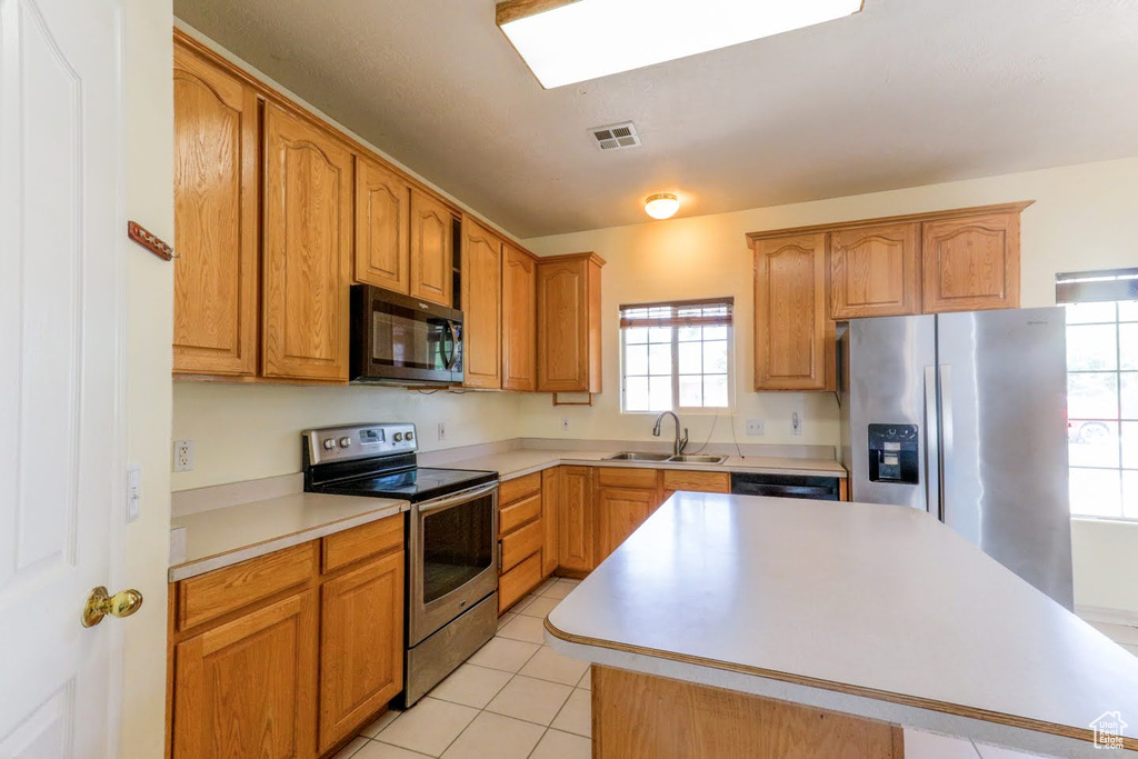 Kitchen with sink, a kitchen island, appliances with stainless steel finishes, and light tile patterned floors