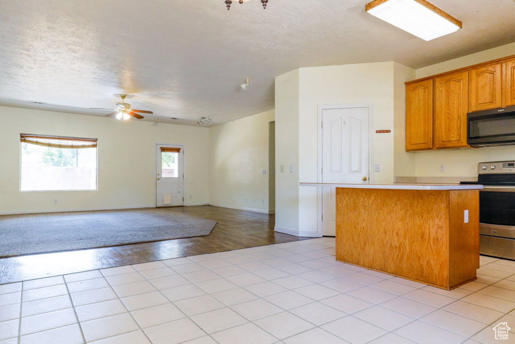 Kitchen with electric stove, light tile patterned floors, and ceiling fan