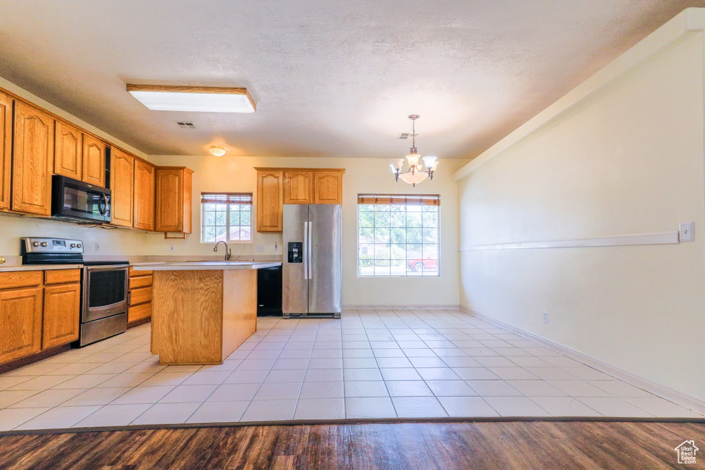 Kitchen with stainless steel appliances, a notable chandelier, a kitchen island, and light wood-type flooring