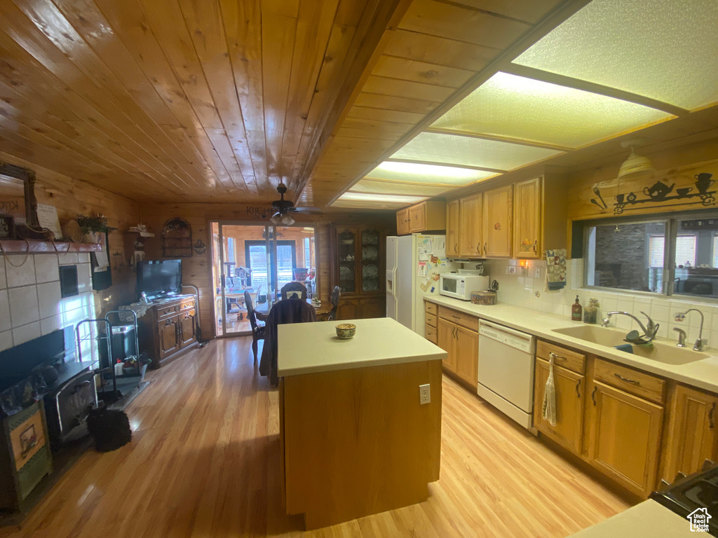 Kitchen with white appliances, sink, light hardwood / wood-style floors, a center island, and wood walls