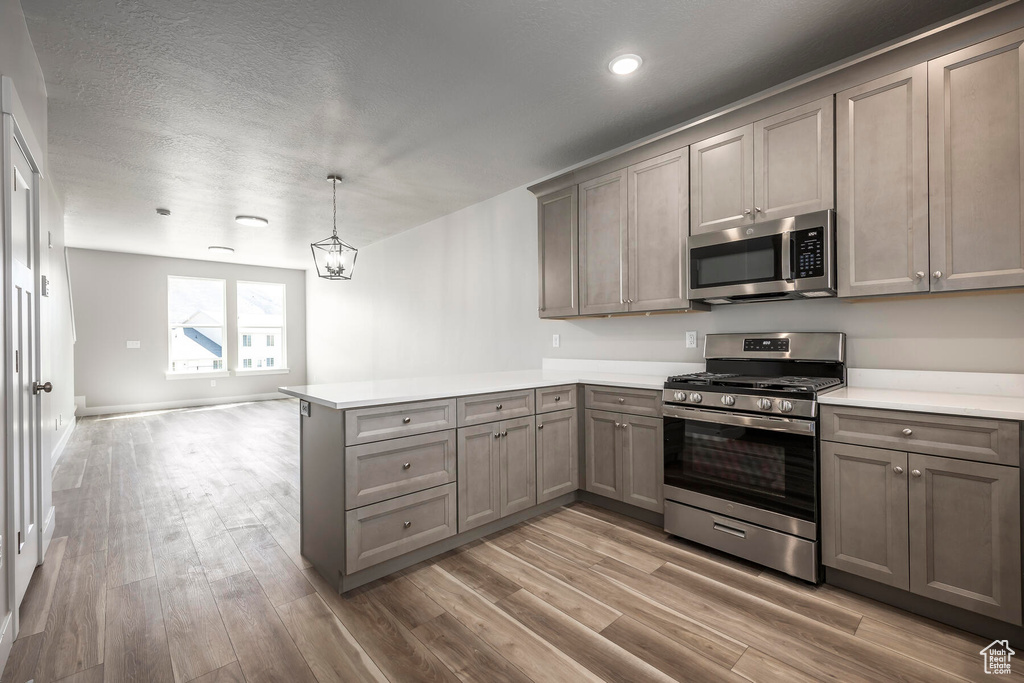 Kitchen with stainless steel appliances, wood-type flooring, hanging light fixtures, and kitchen peninsula