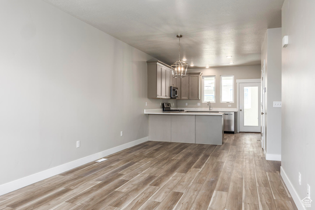 Kitchen featuring an inviting chandelier, kitchen peninsula, light hardwood / wood-style floors, appliances with stainless steel finishes, and gray cabinetry