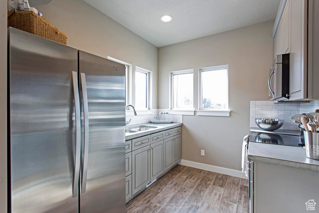 Kitchen with sink, light hardwood / wood-style floors, appliances with stainless steel finishes, backsplash, and gray cabinetry