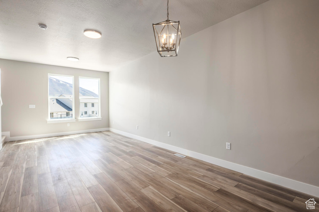 Unfurnished room with an inviting chandelier, a textured ceiling, and hardwood / wood-style flooring