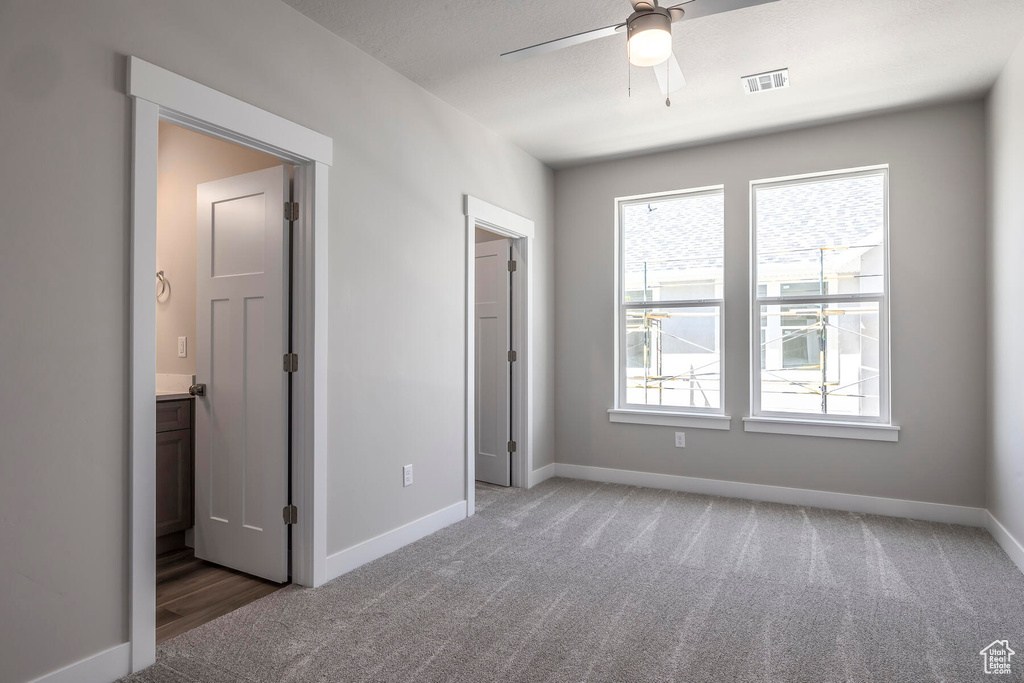 Unfurnished bedroom with carpet floors, ensuite bathroom, and ceiling fan