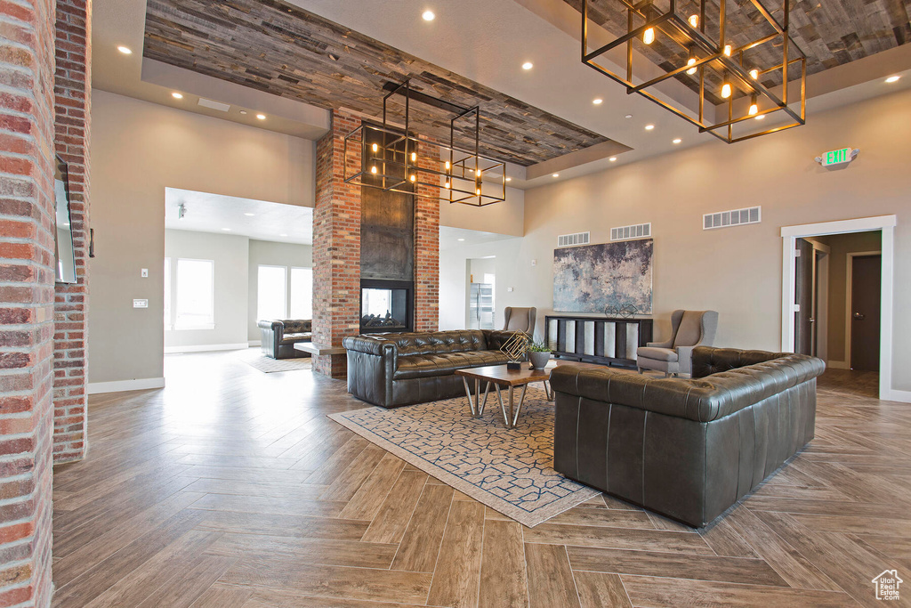 Living room featuring parquet flooring, a brick fireplace, brick wall, a towering ceiling, and a raised ceiling