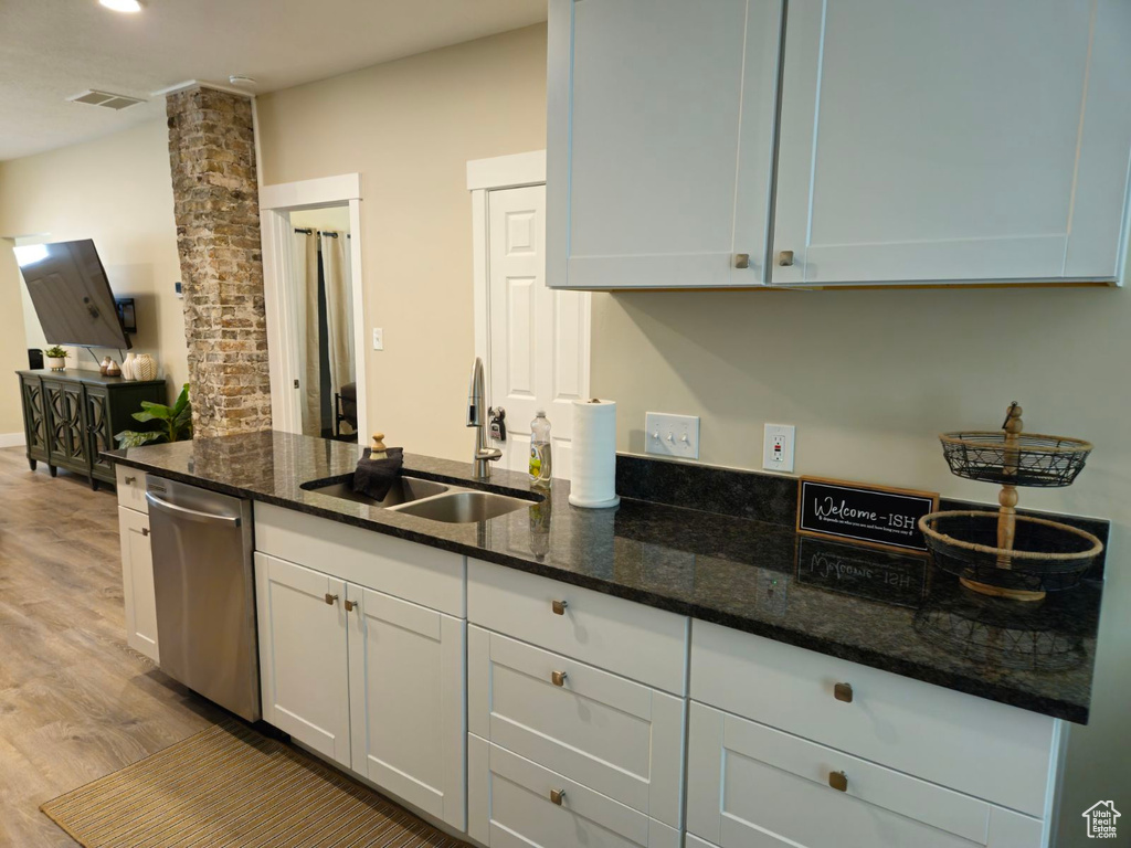 Kitchen with white cabinets, sink, stainless steel dishwasher, light wood-type flooring, and dark stone countertops